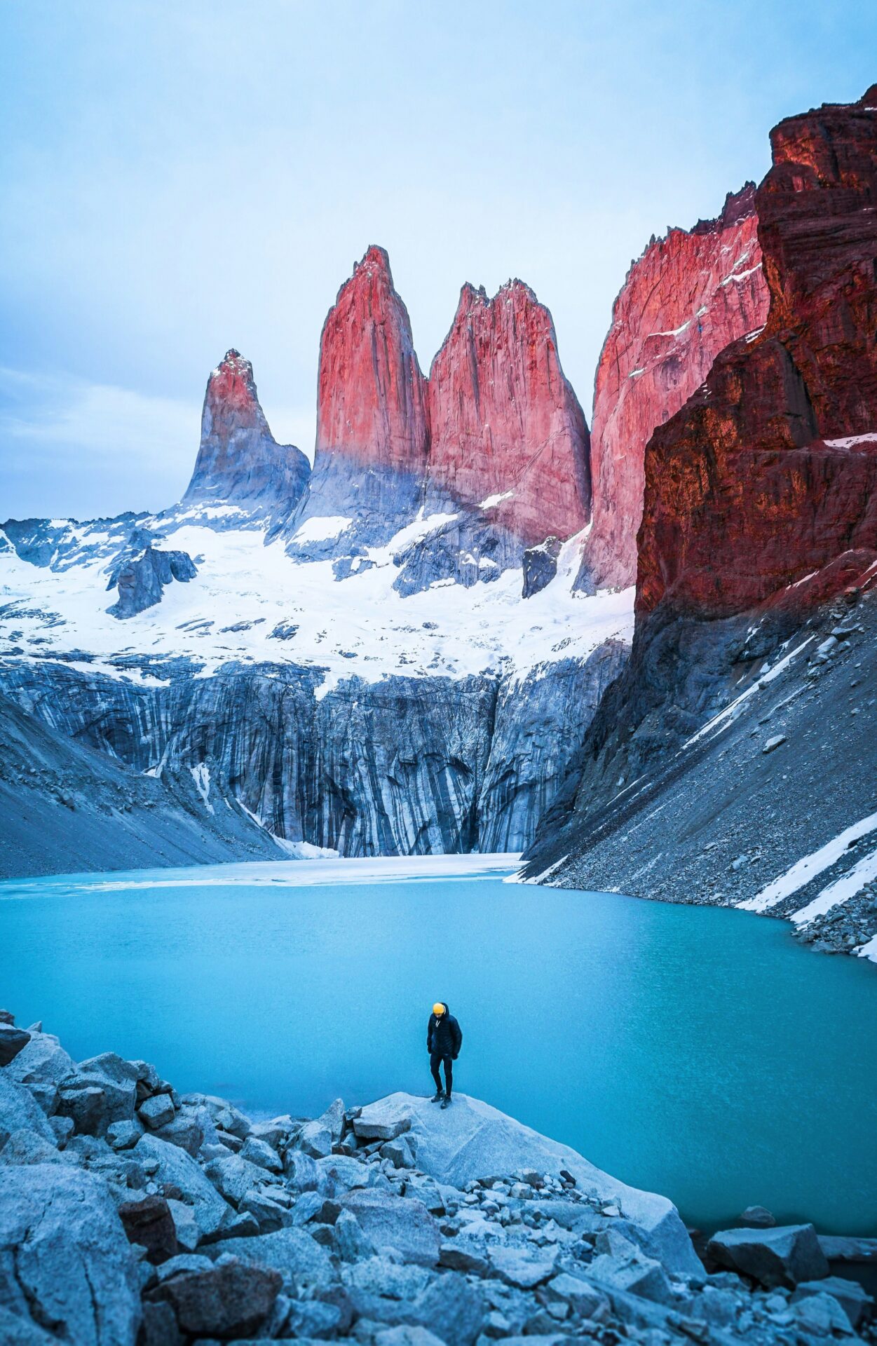 man standing on rock facing body of water and mountain